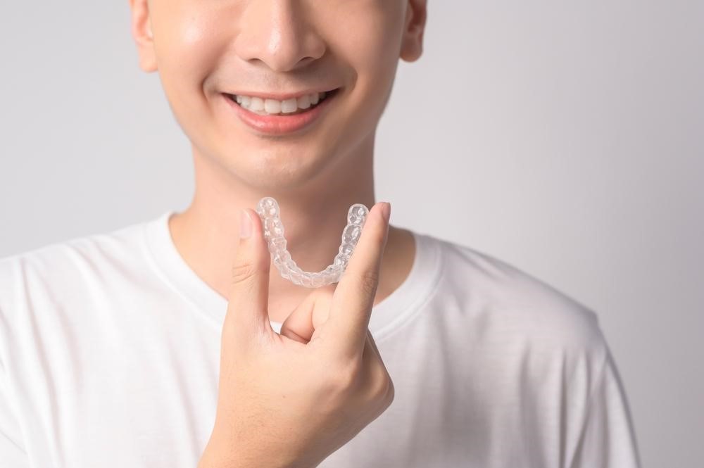 young smiling man holding invisalign braces